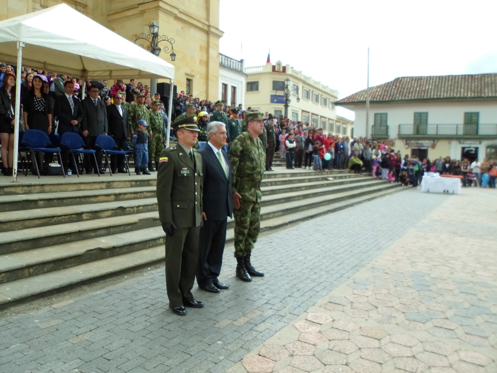 Desfile cívico-militar en la plaza principal de un municipio, presidido por autoridades civiles, militares y de policía